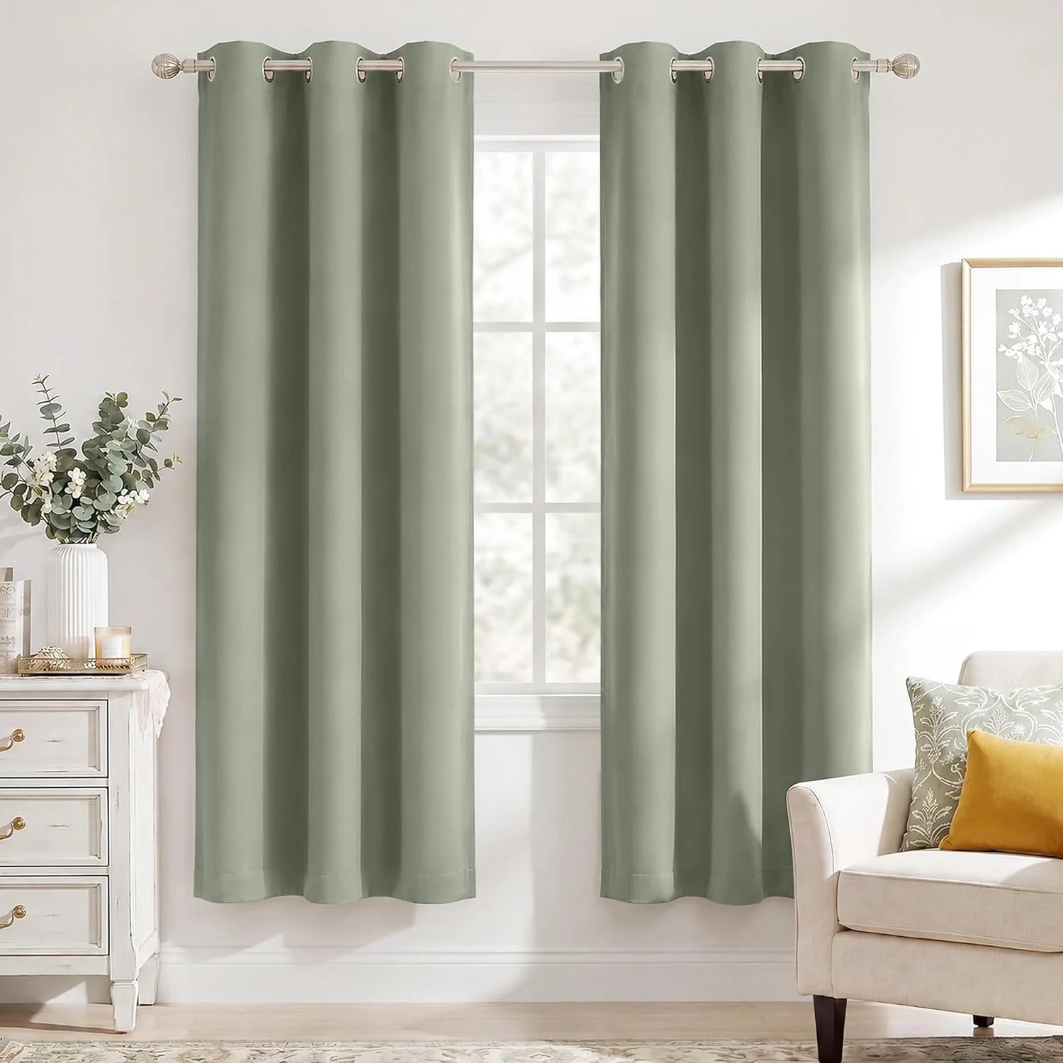 Sage green grommet top blackout curtains hanging in a bright, modern living room with a white armchair and dresser.