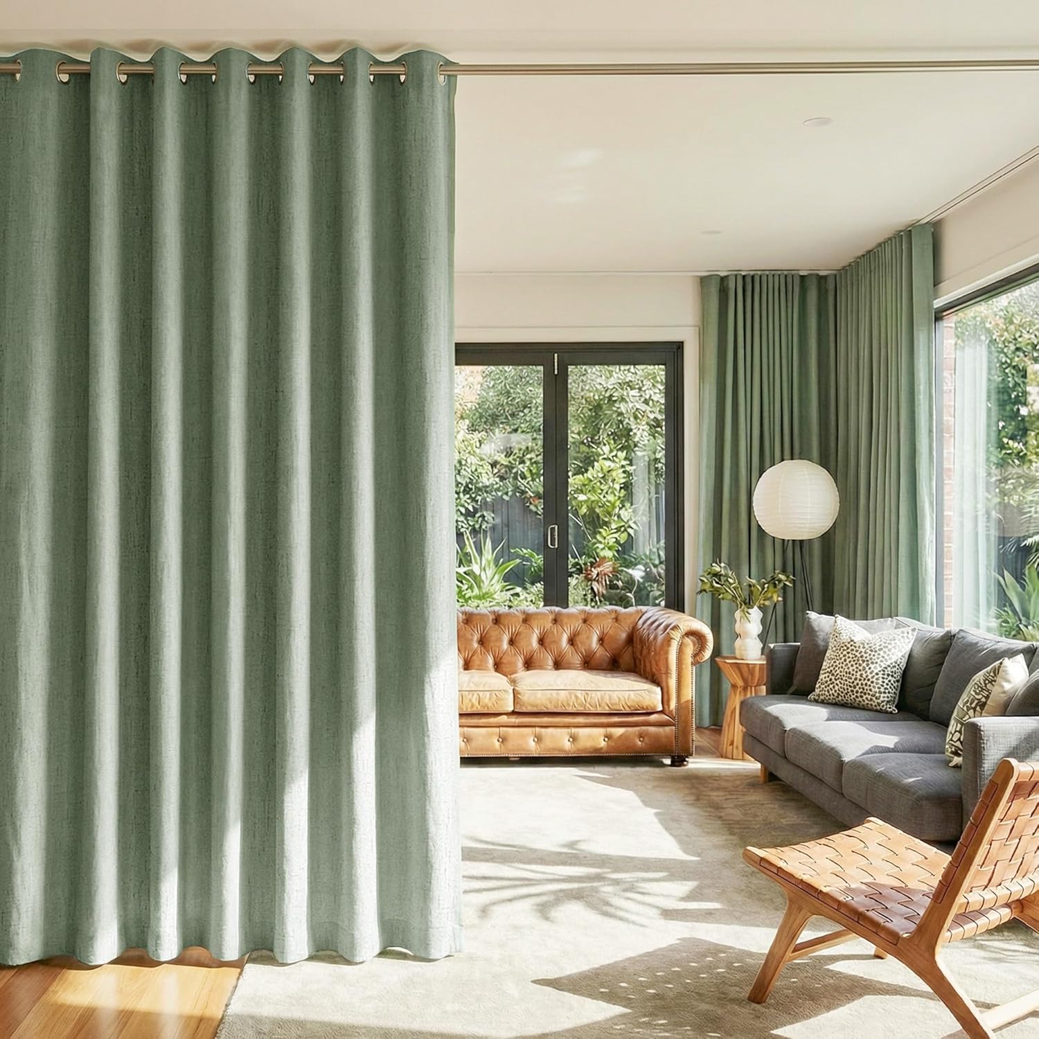 Textured sage green grommet-top curtain creating a division in a sunlit, modern living room.