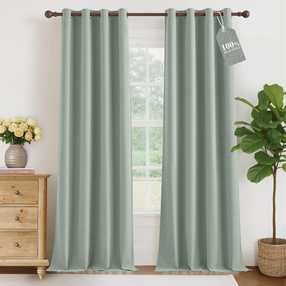 Pair of sage green textured blackout curtains with grommet top hanging on a wooden rod in a room.