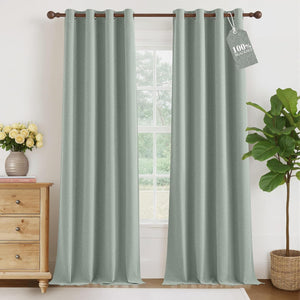 Pair of sage green textured blackout curtains with grommet top hanging on a wooden rod in a room.