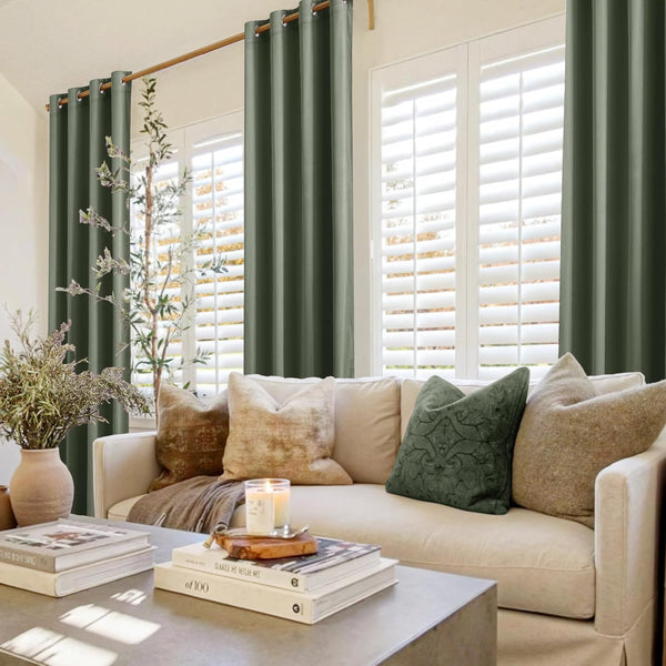 Sage green solid grommet top drapes hanging on a wooden rod in a bright living room