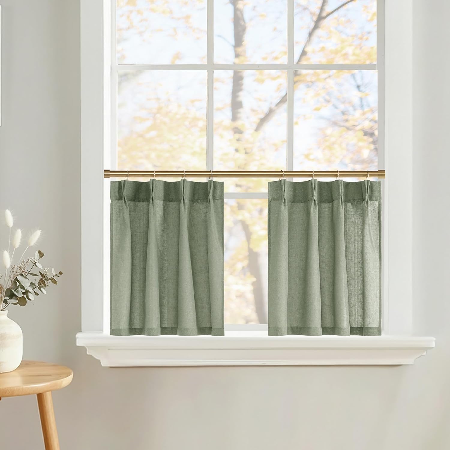 Sage green linen blend cafe curtains hanging on a brass rod, offering light filtering privacy in a bright room.