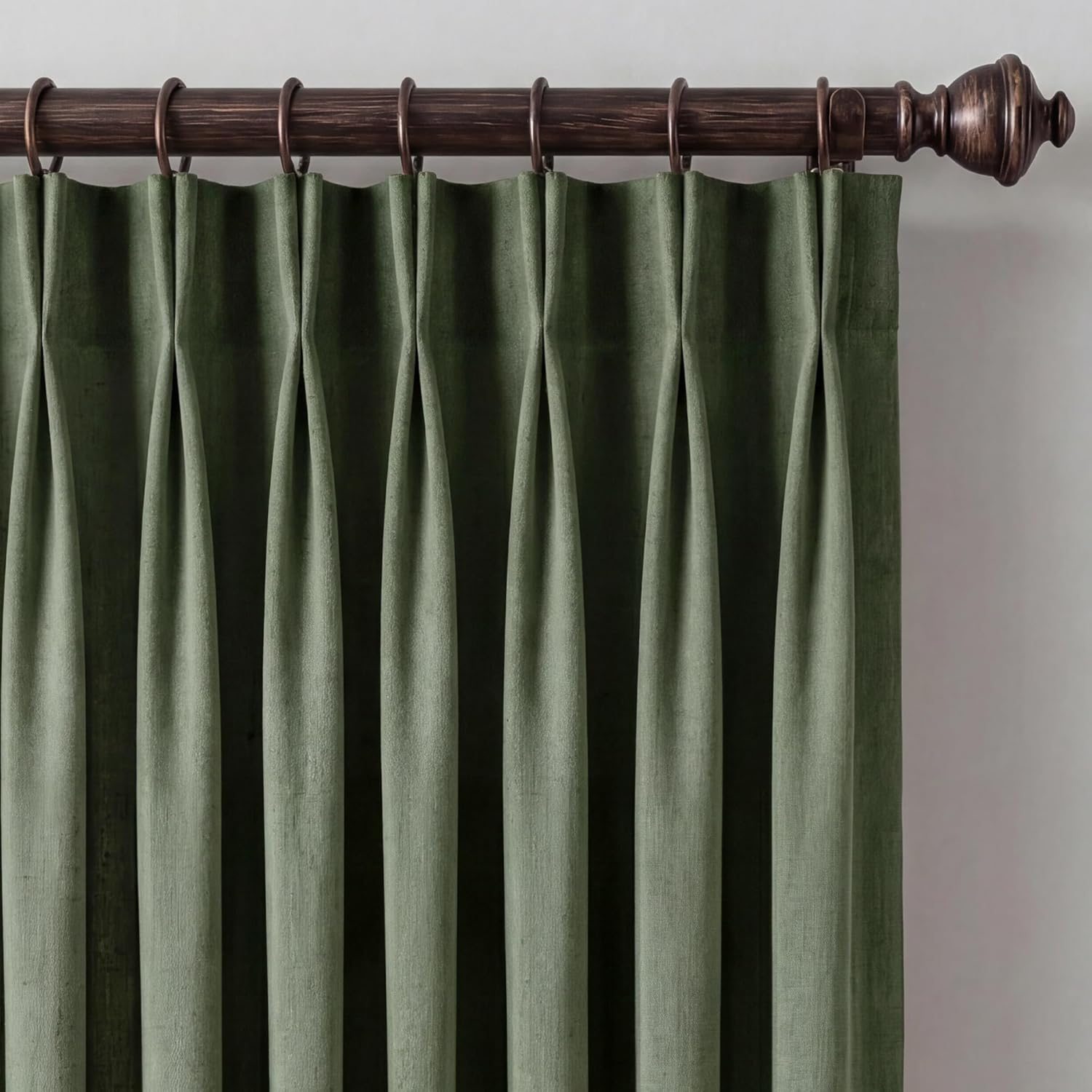 Textured sage green curtain panel with triple pinch pleats on a decorative bronze rod.
