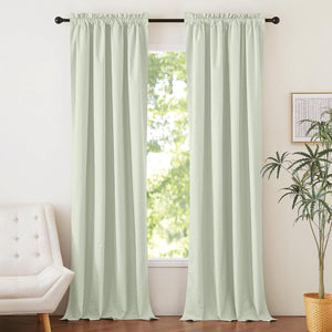 Pair of light sage green rod pocket curtains hang on a black rod, framing a bright window.