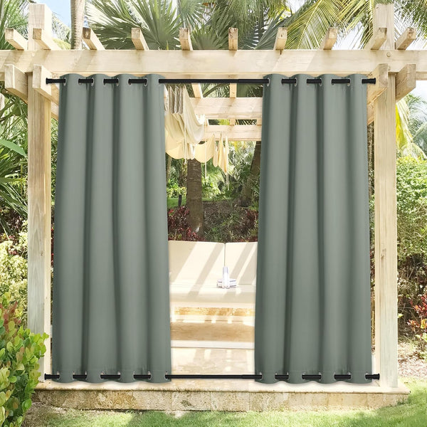 Pair of sage green outdoor grommet top curtains on a pergola patio surrounded by tropical plants.