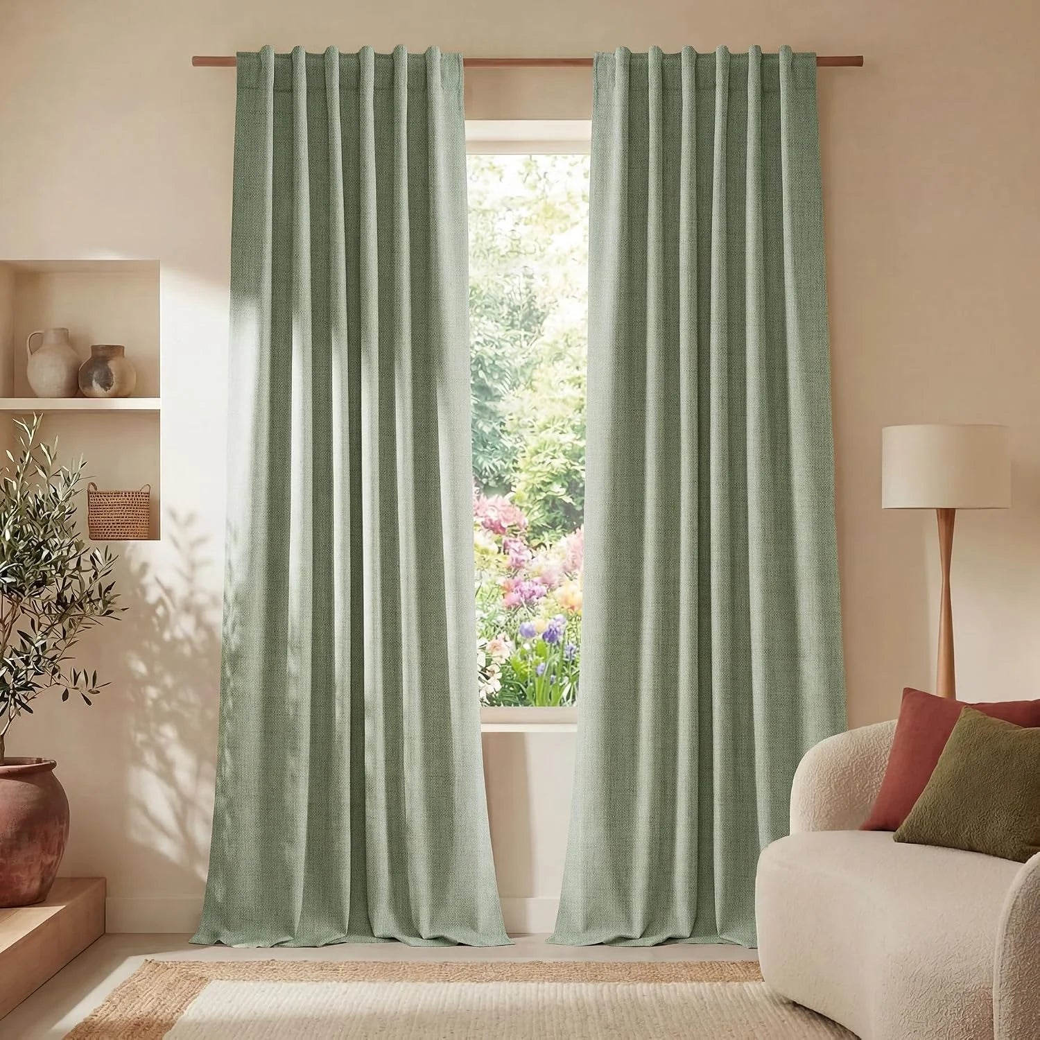 Sage green pinch pleat curtains on a wooden rod in a bright living room with outdoor garden view.