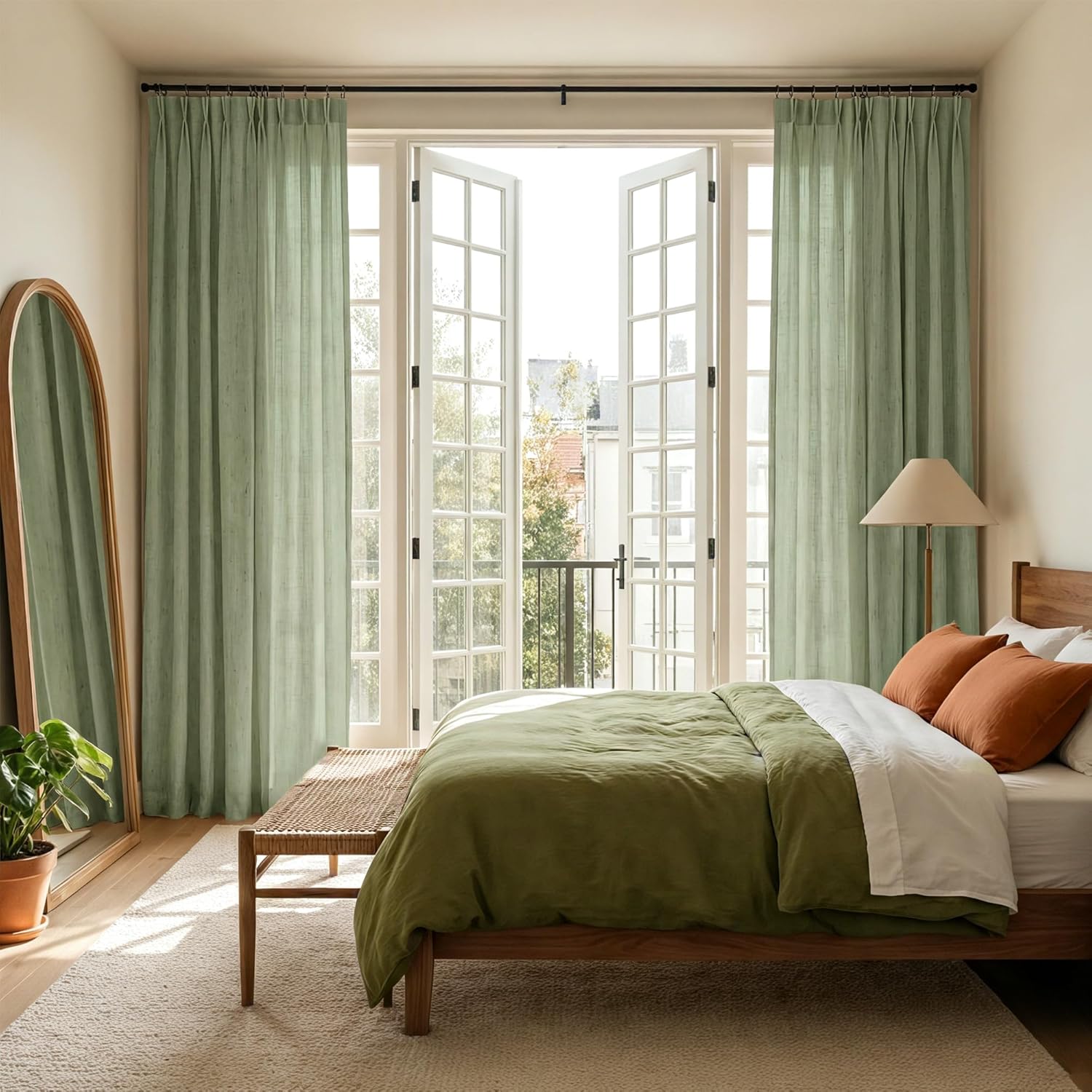 Light sage green pinch pleat linen curtains hanging over open French doors in a bright bedroom.