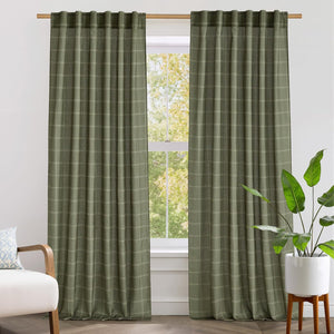 Textured sage green plaid drapes with pinch pleat top hang on a wooden rod by a sunlit window.