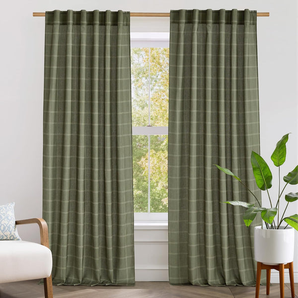 Textured sage green plaid drapes with pinch pleat top hang on a wooden rod by a sunlit window.