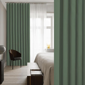 Sage green pleated blackout curtains with ring top hanging in a bright modern bedroom.