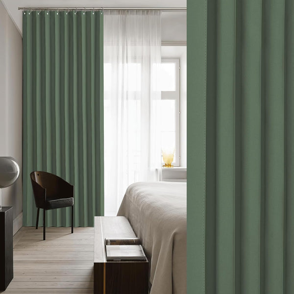 Sage green pleated blackout curtains with ring top hanging in a bright modern bedroom.