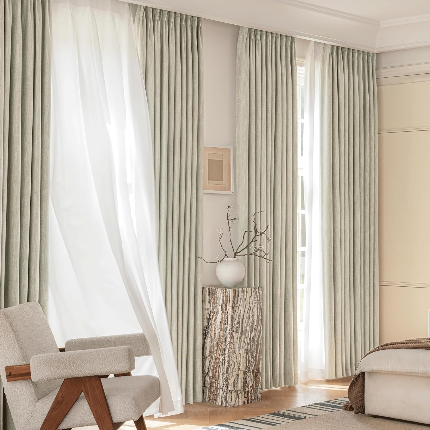 Sage green pleated drapes and sheer white curtains hang over a large window in a bright room.