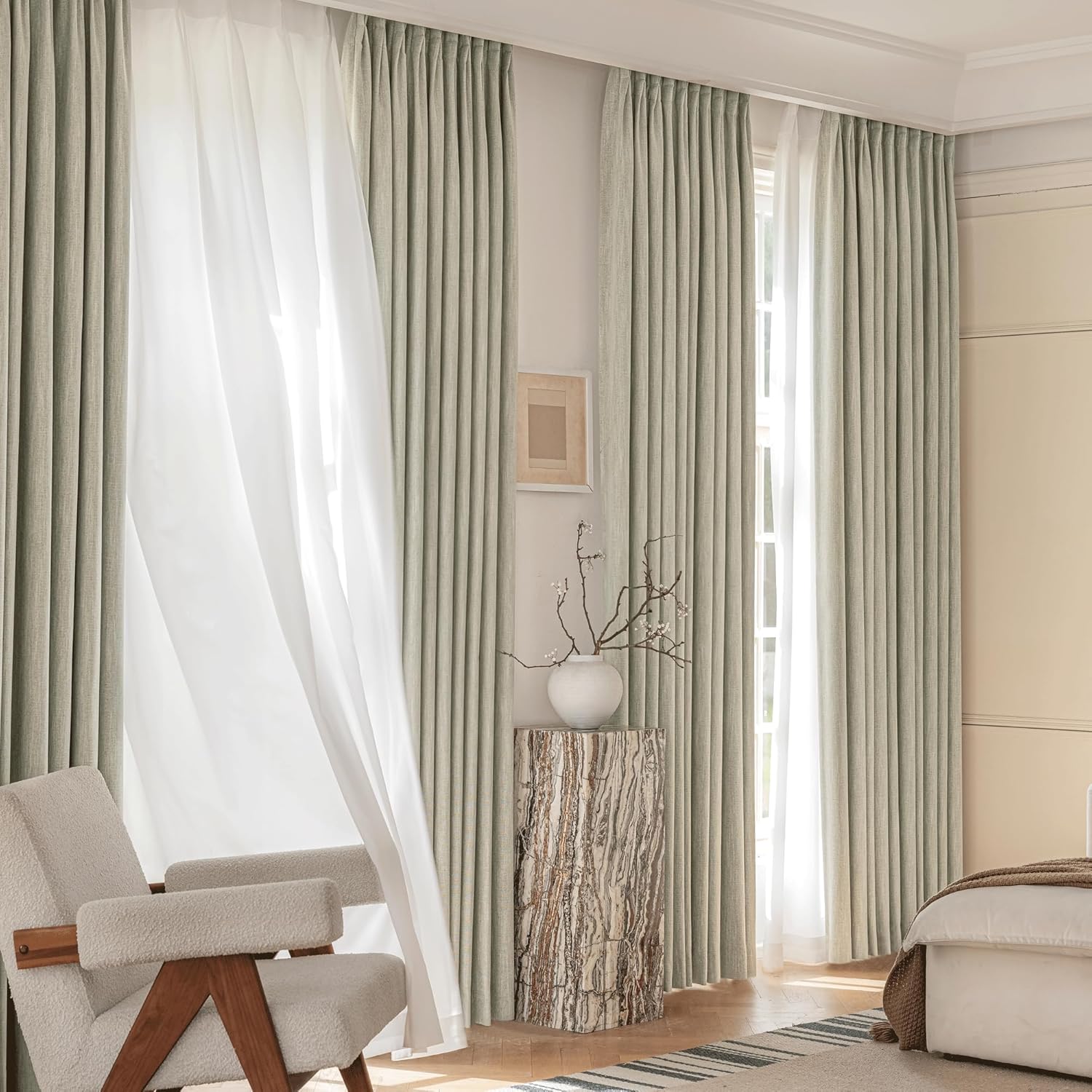 Full-length sage green pleated drapes and white sheer curtains hang in a serene bedroom with natural light.