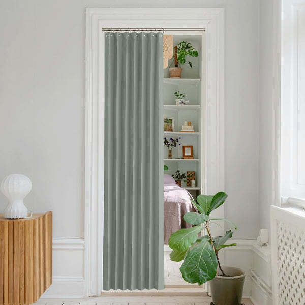 Sage green pleated fabric doorway curtain on a rod with rings. Partially shows a room with shelves.