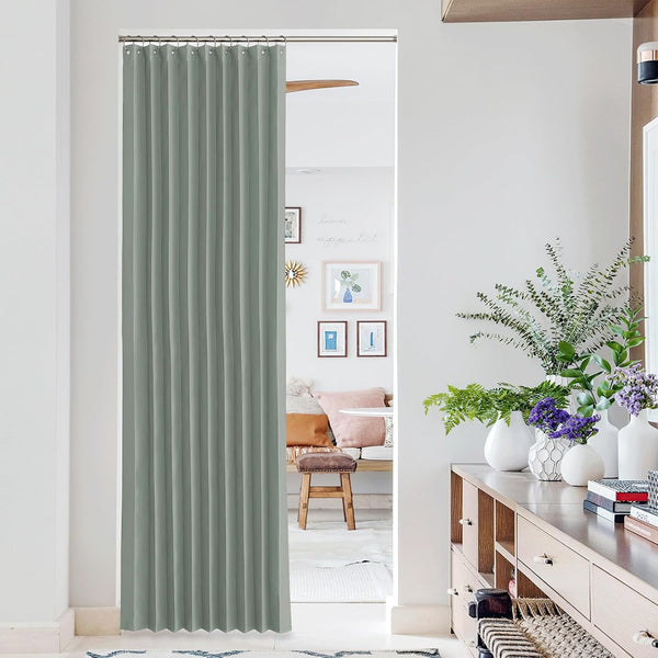 Sage green pleated fabric room divider curtain hanging from a tension rod in a hallway opening.