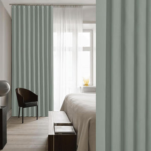 Sage green pleated window curtains hang on a rod in a bright bedroom, paired with sheer white drapes.