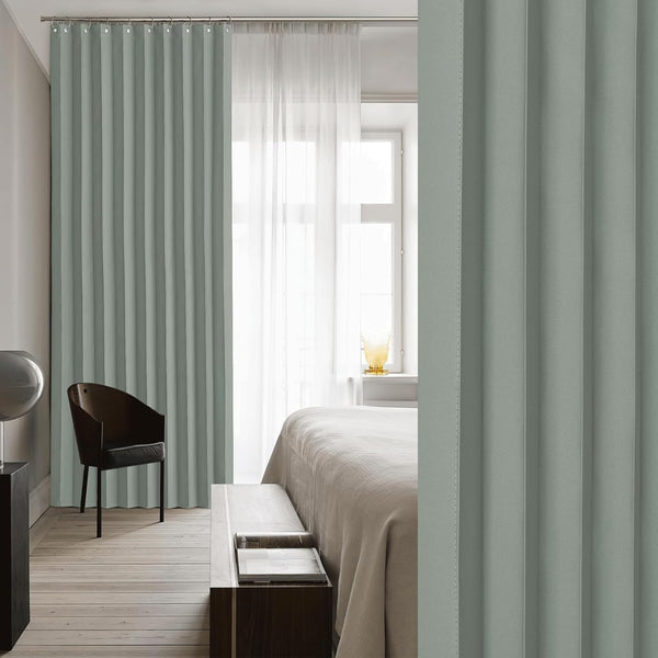 Sage green pleated window curtains hang on a rod in a bright bedroom, paired with sheer white drapes.