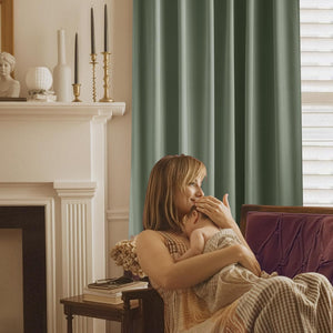Muted sage green pleated room darkening curtain hanging by a window in a cozy living room.