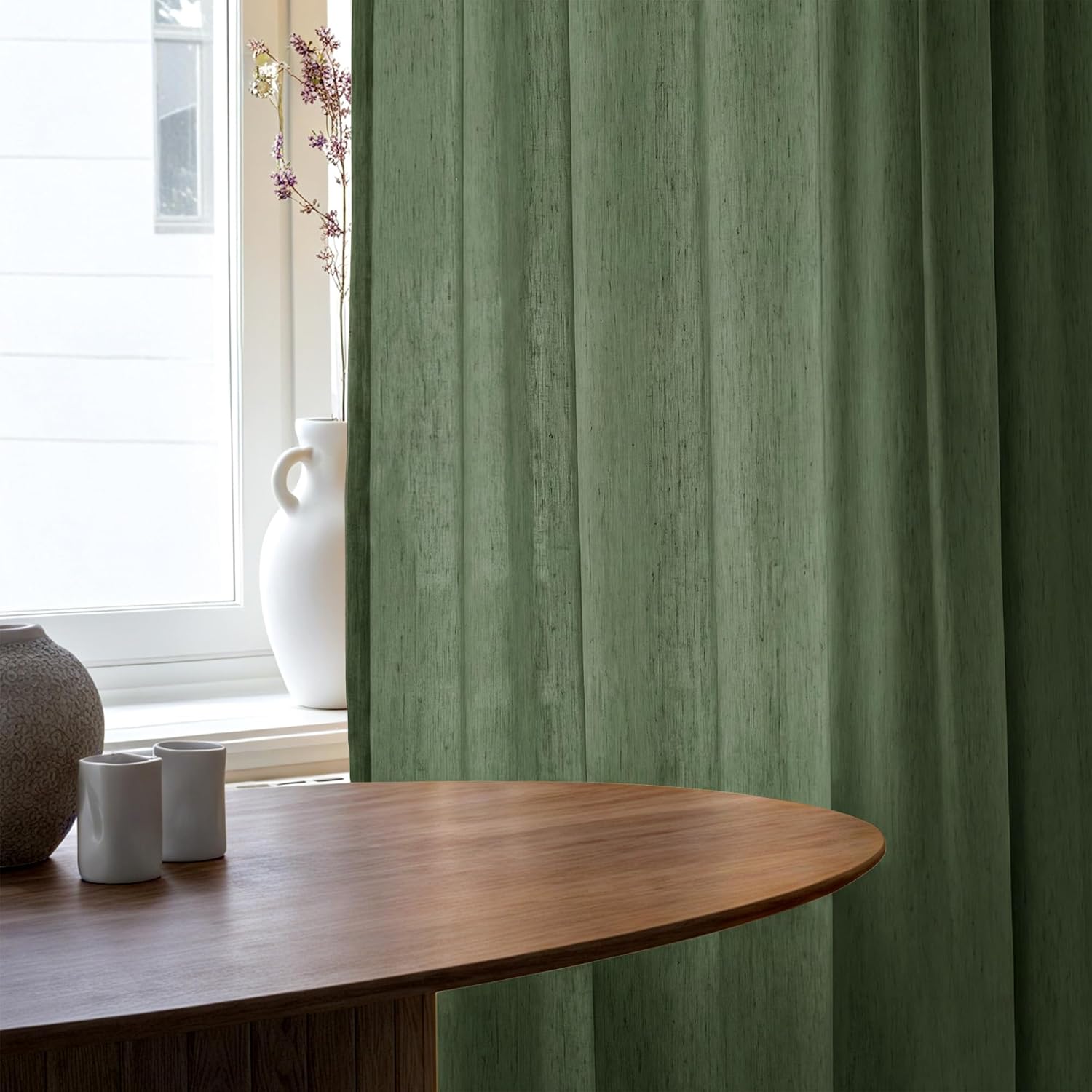 Sage green slub weave semi-sheer curtains hanging gracefully by a sunlit window.