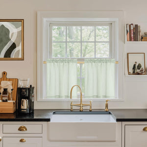Sage green and white vertically striped ruffled tier curtains hanging on a gold rod in a bright kitchen window.