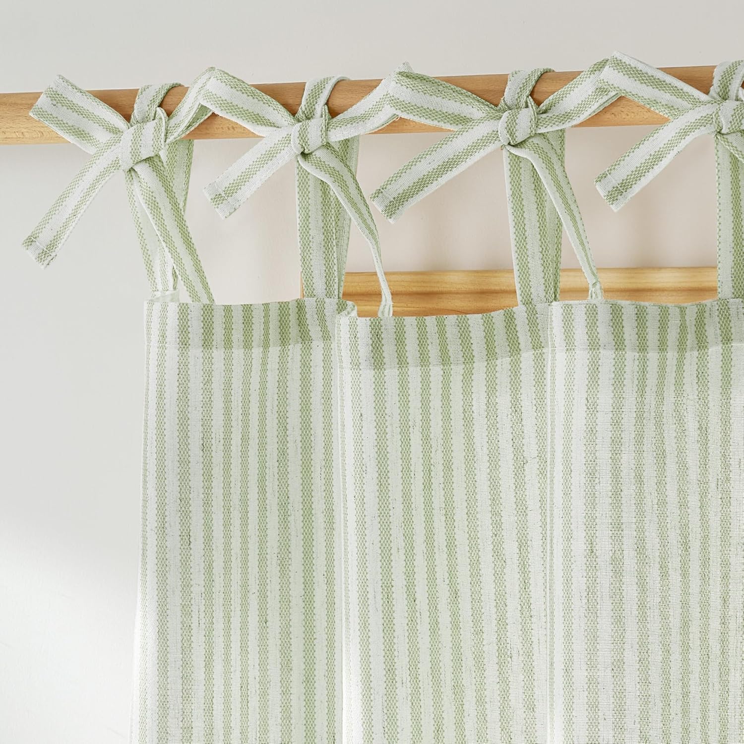 Sage green and white striped tie-top window curtains with a textured weave hanging on a wooden rod.