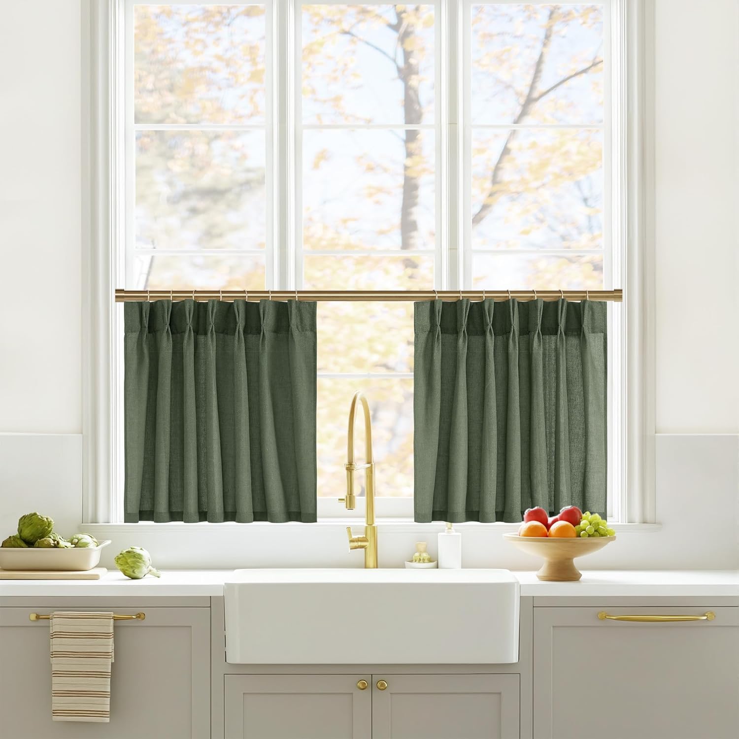 Sage green textured cafe curtains with pleats hanging on a brass rod in a bright kitchen window.