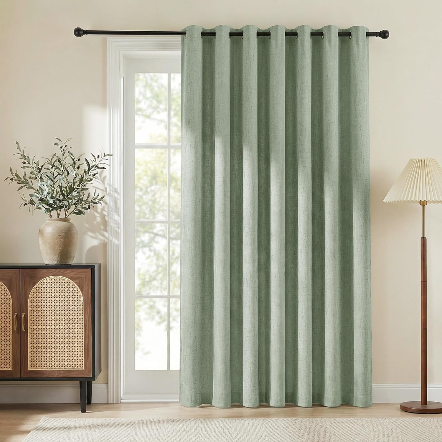 Sage green curtain panel with a textured fabric and grommet top, hanging on a black rod over a glass door.