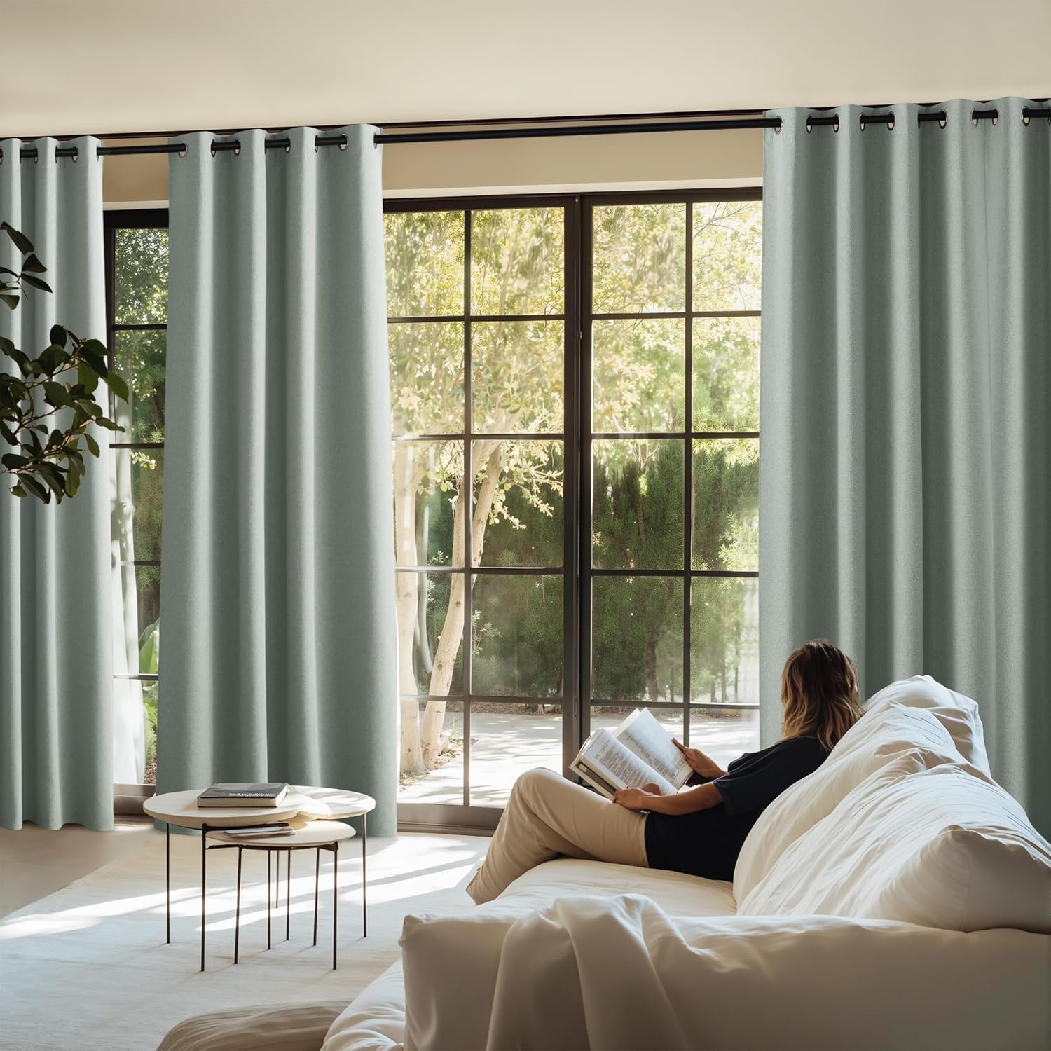 Sage green textured grommet top curtains on a black rod, framing large windows in a modern living room.