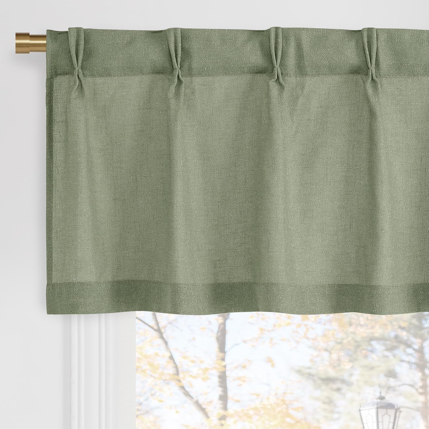 Textured sage green pinch pleat valance hanging on a brass curtain rod over a window.