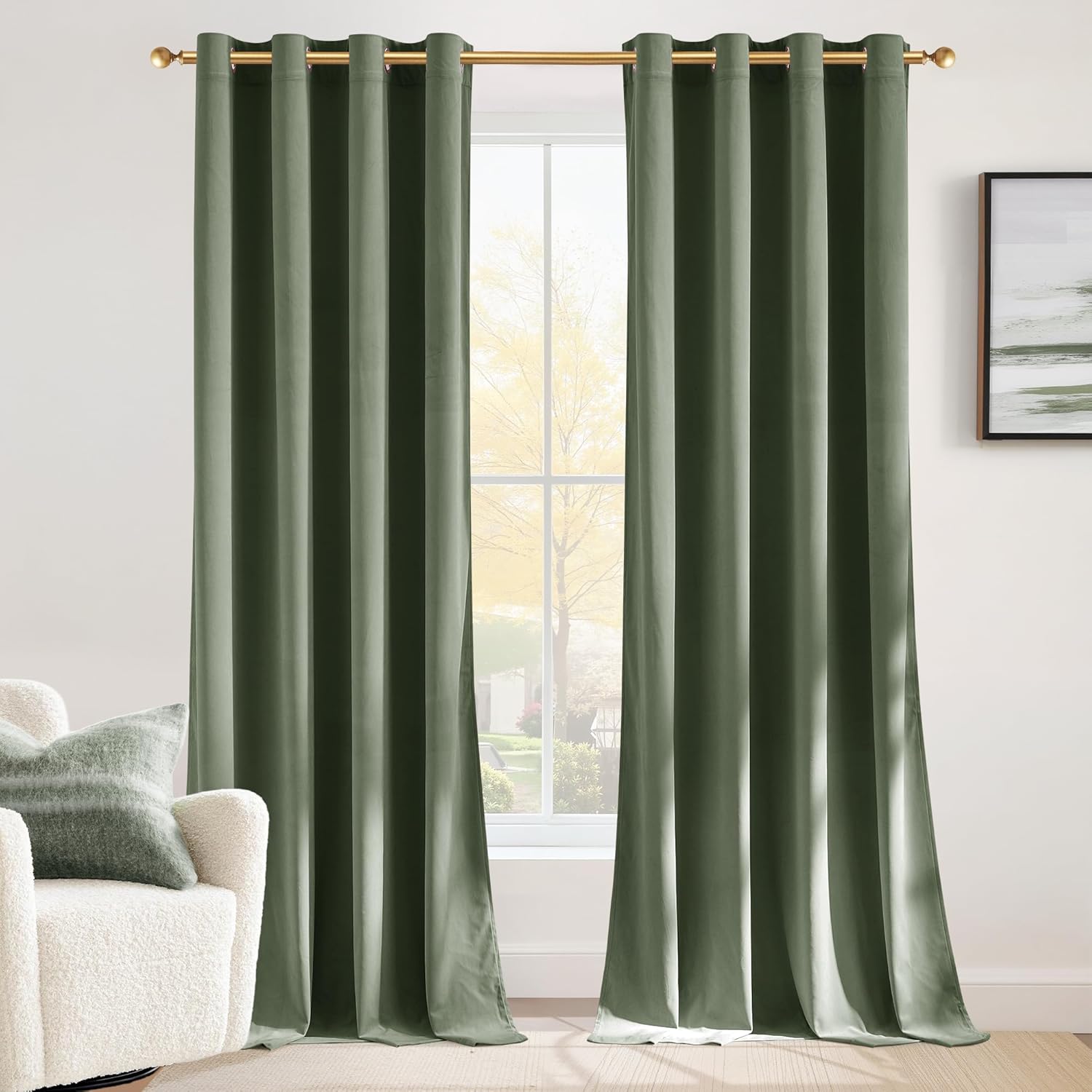 Two sage green velvet blackout curtains with gold grommets hanging on a window rod in a modern room.