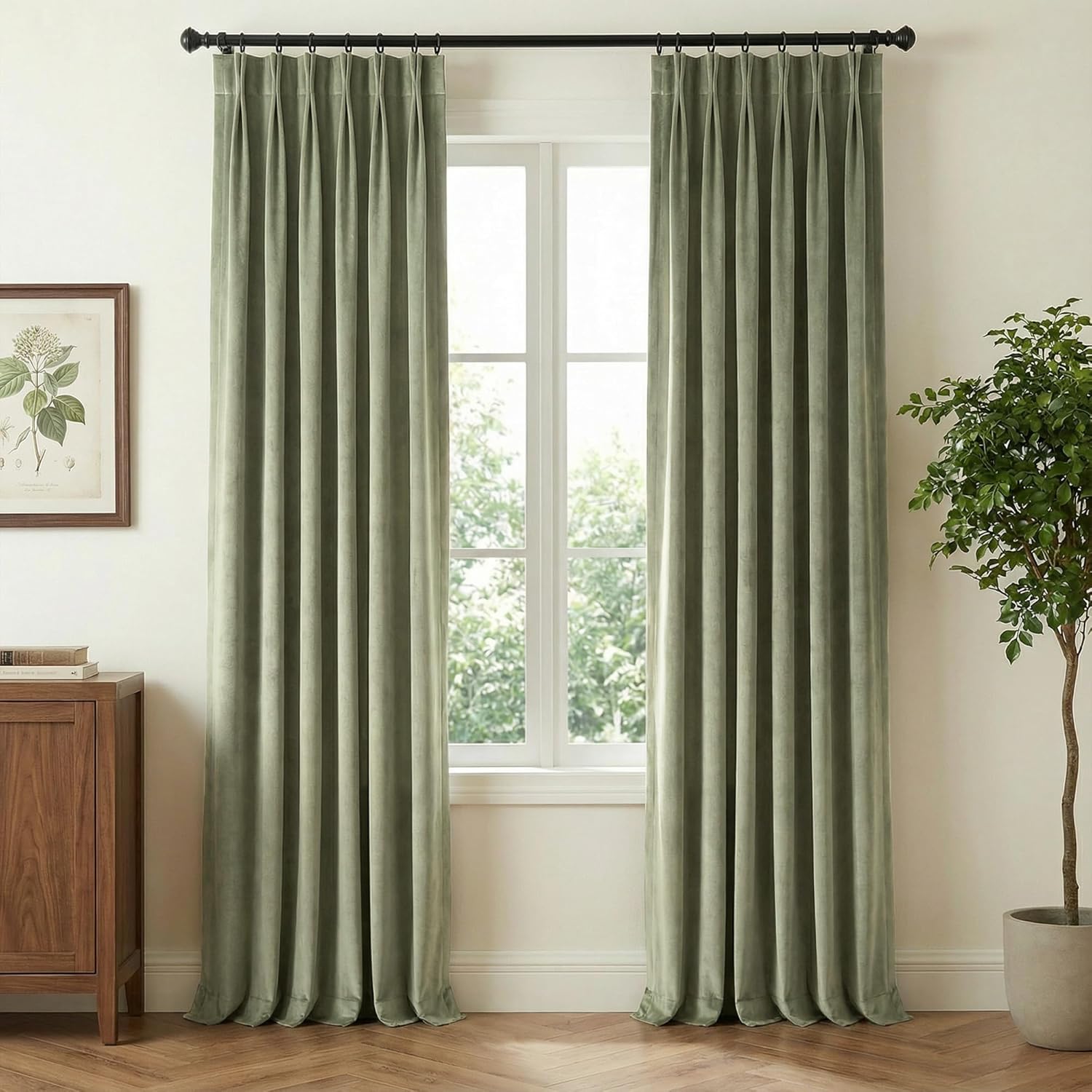 Long sage green velvet pinch pleat curtains hanging on a black rod, framing a window.