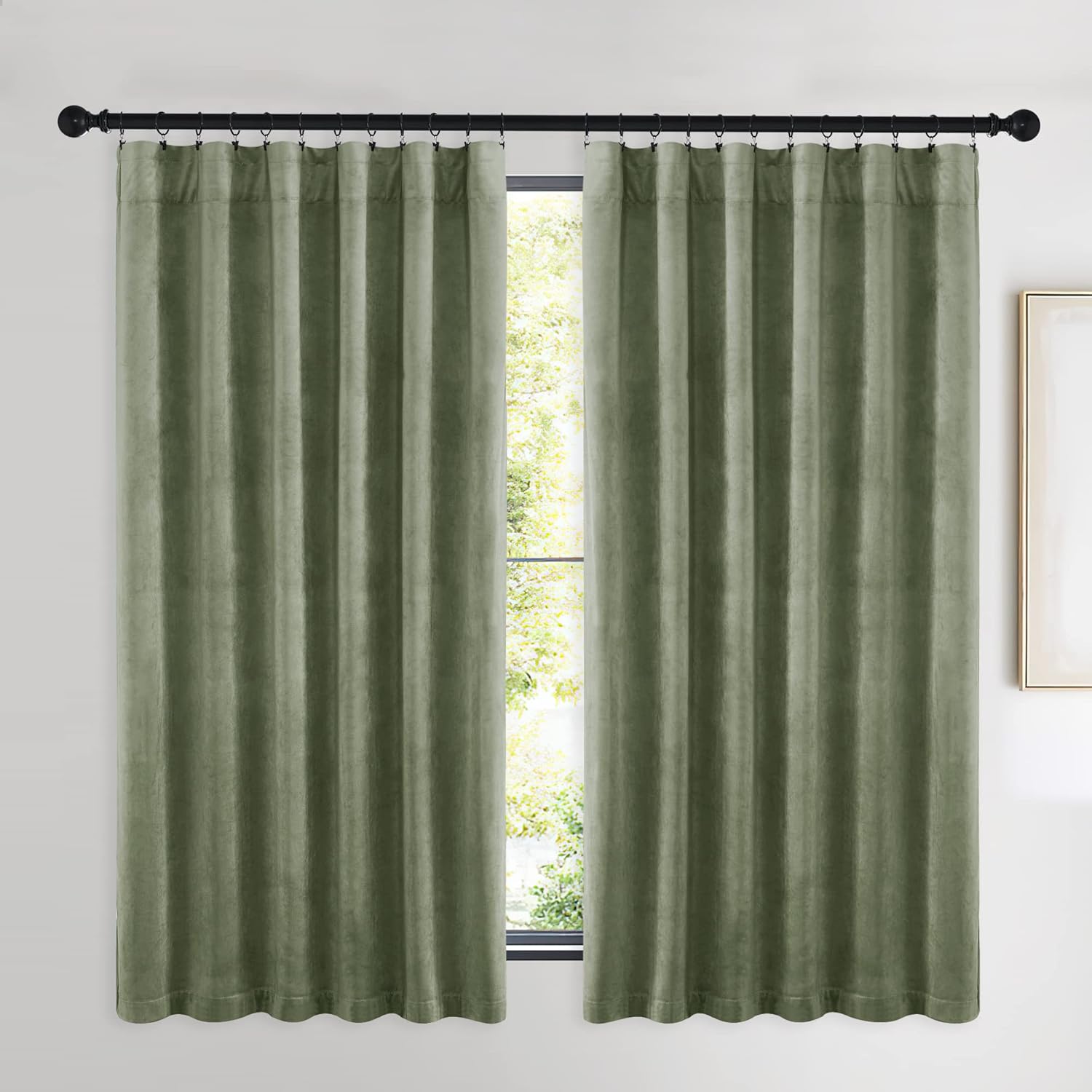 Pair of sage green velvet curtains with ring top header hanging on a black rod over a window.