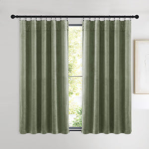 Soft sage green velvet curtains hung by rings on a black rod, framing a bright window with lush trees outside.