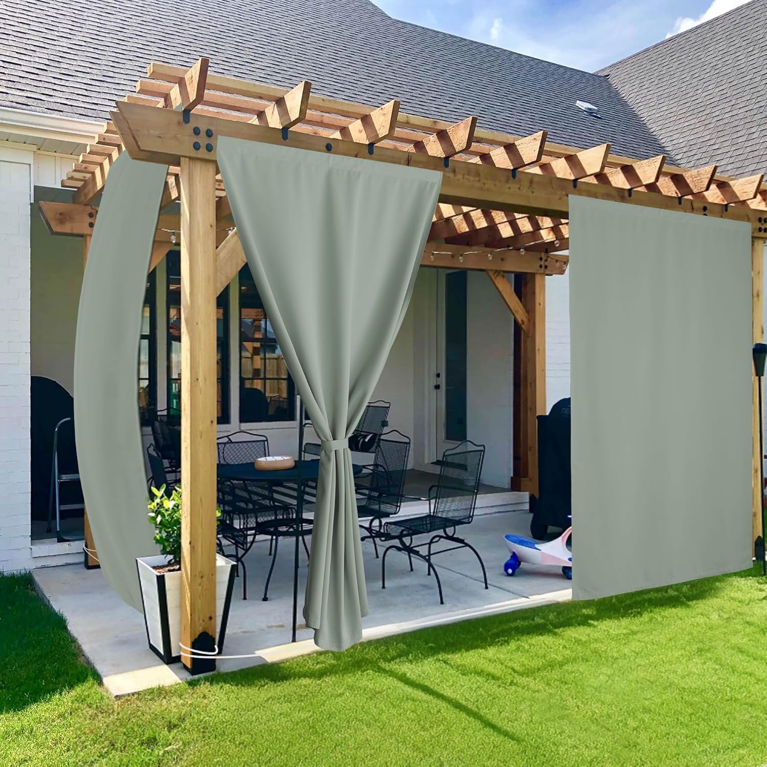 Sage grey outdoor privacy curtains hanging on a rustic wooden pergola over a backyard patio dining set.