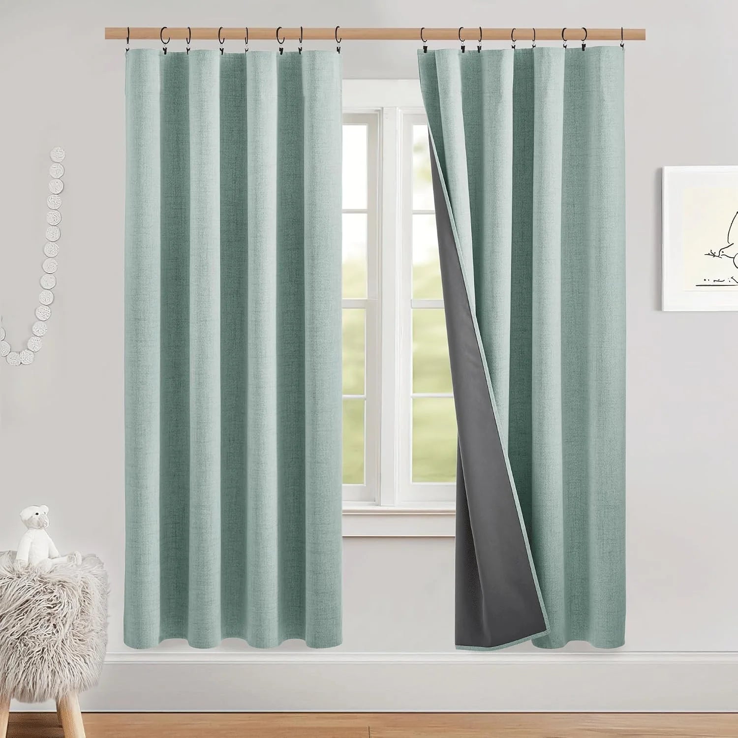 Sage green linen-look blackout curtains with ring top on a wood rod in a bright nursery