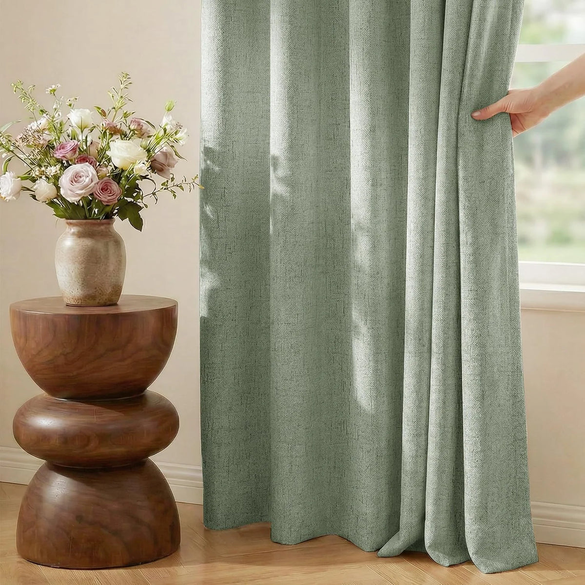 Sage green linen-look curtain panel beside a window with wood side table and flowers
