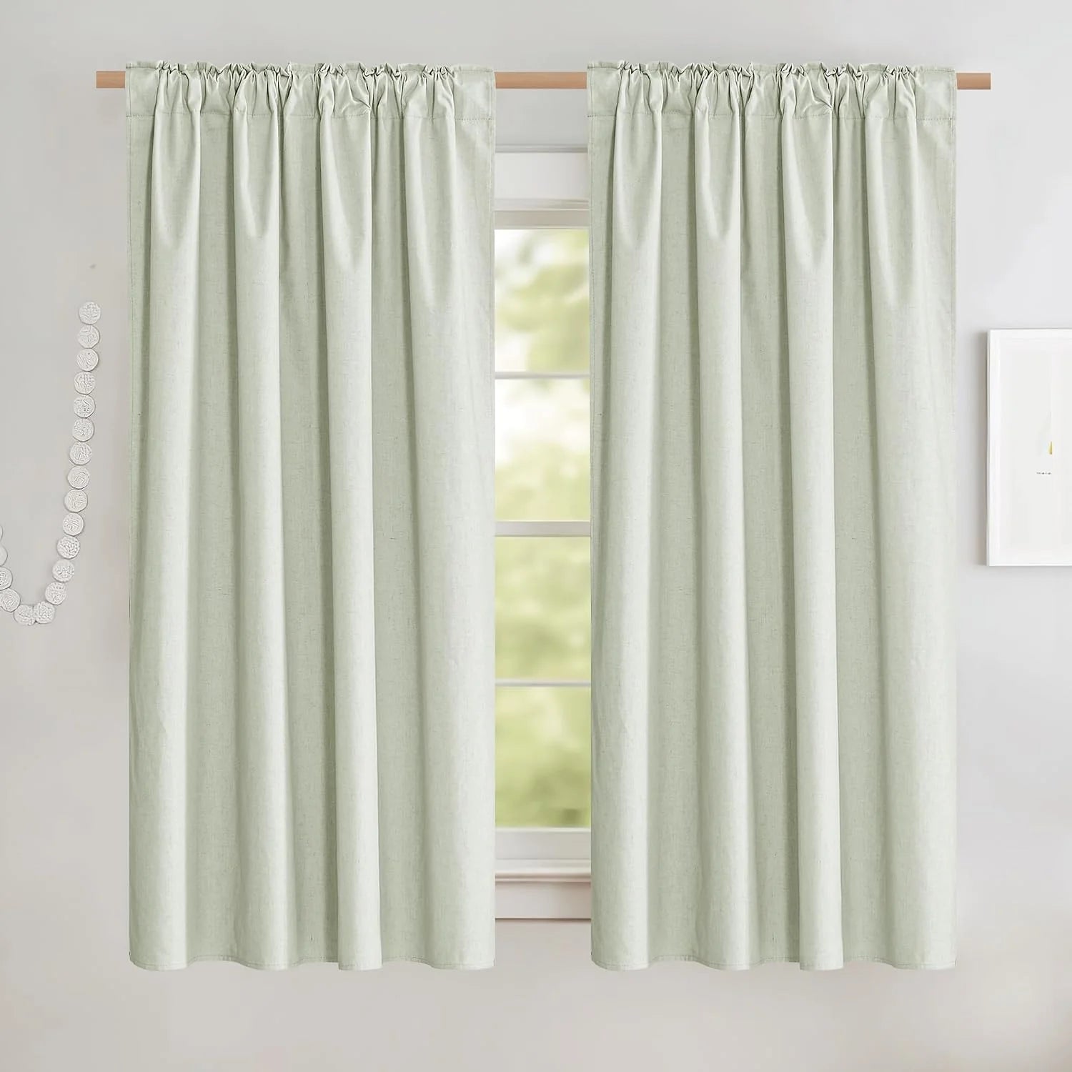 Soft sage green rod pocket curtains hanging on a wooden pole over a bright window