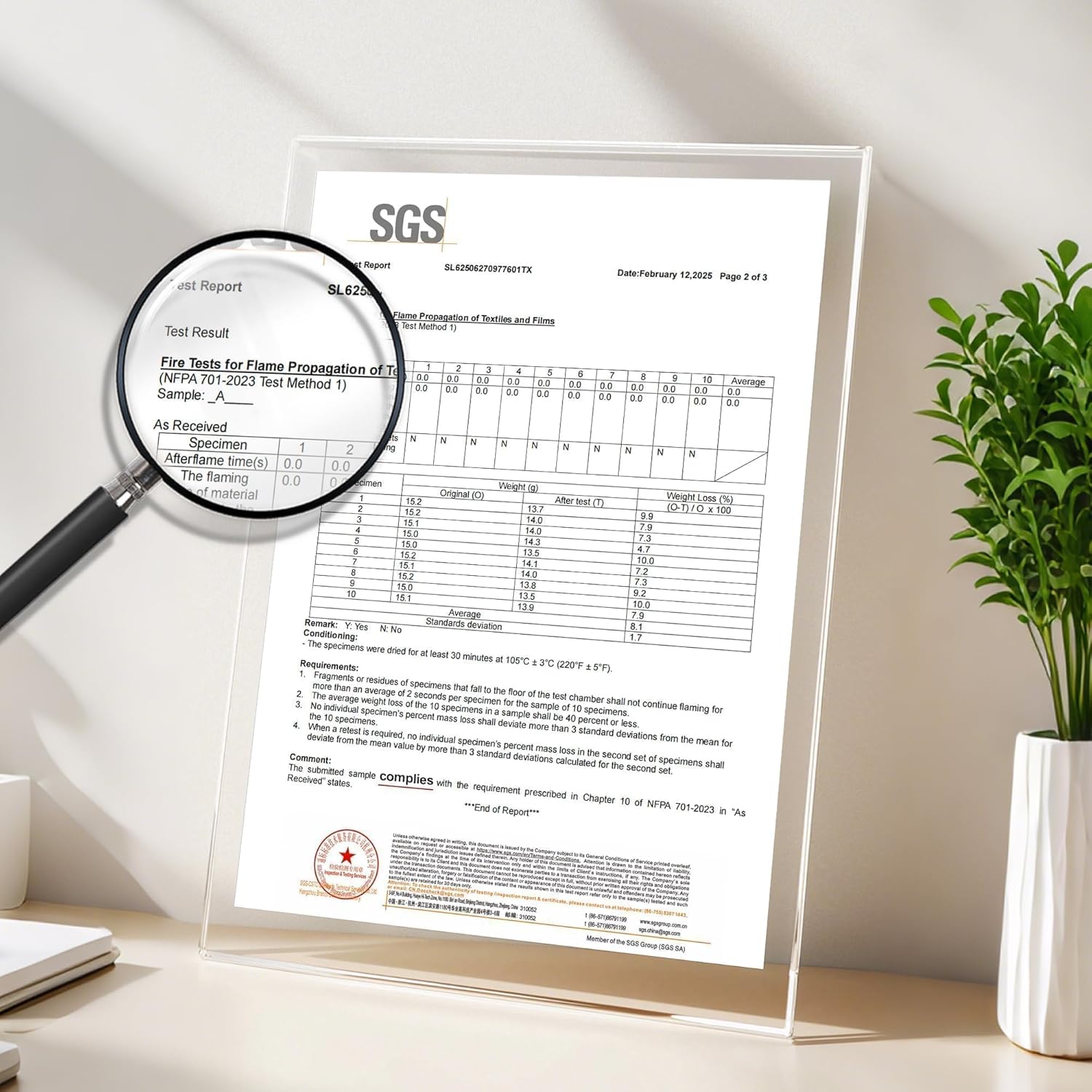 SGS textile fire test report in acrylic stand. Magnifying glass shows NFPA 701 flame compliance.