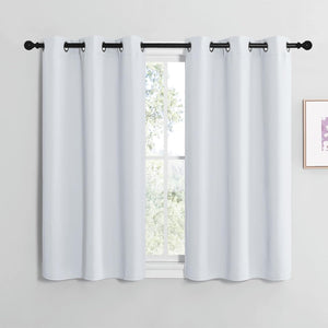 Pair of short white blackout curtains with dark metal grommets hanging on a black rod over a window.