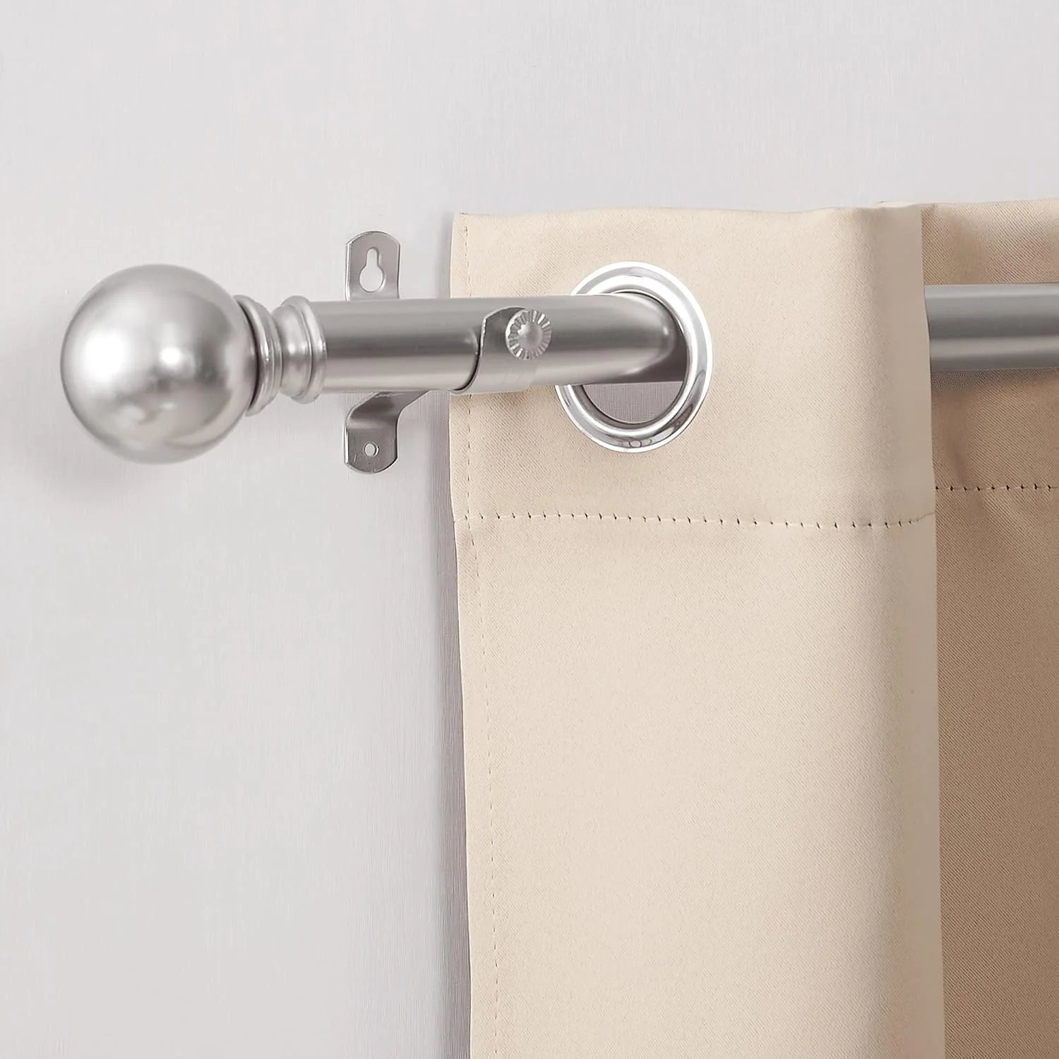 Close-up of a silver curtain rod with round finial and beige grommet curtain