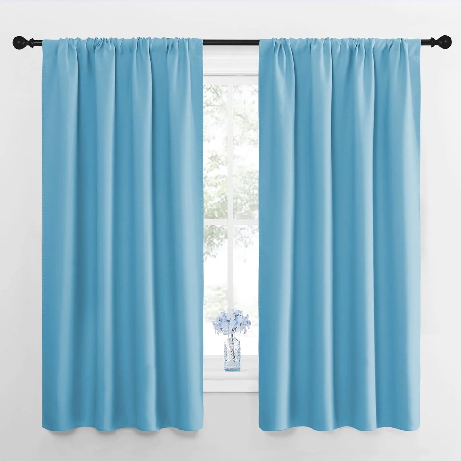 Sky blue rod pocket curtain panels hanging on a black rod over a bright window
