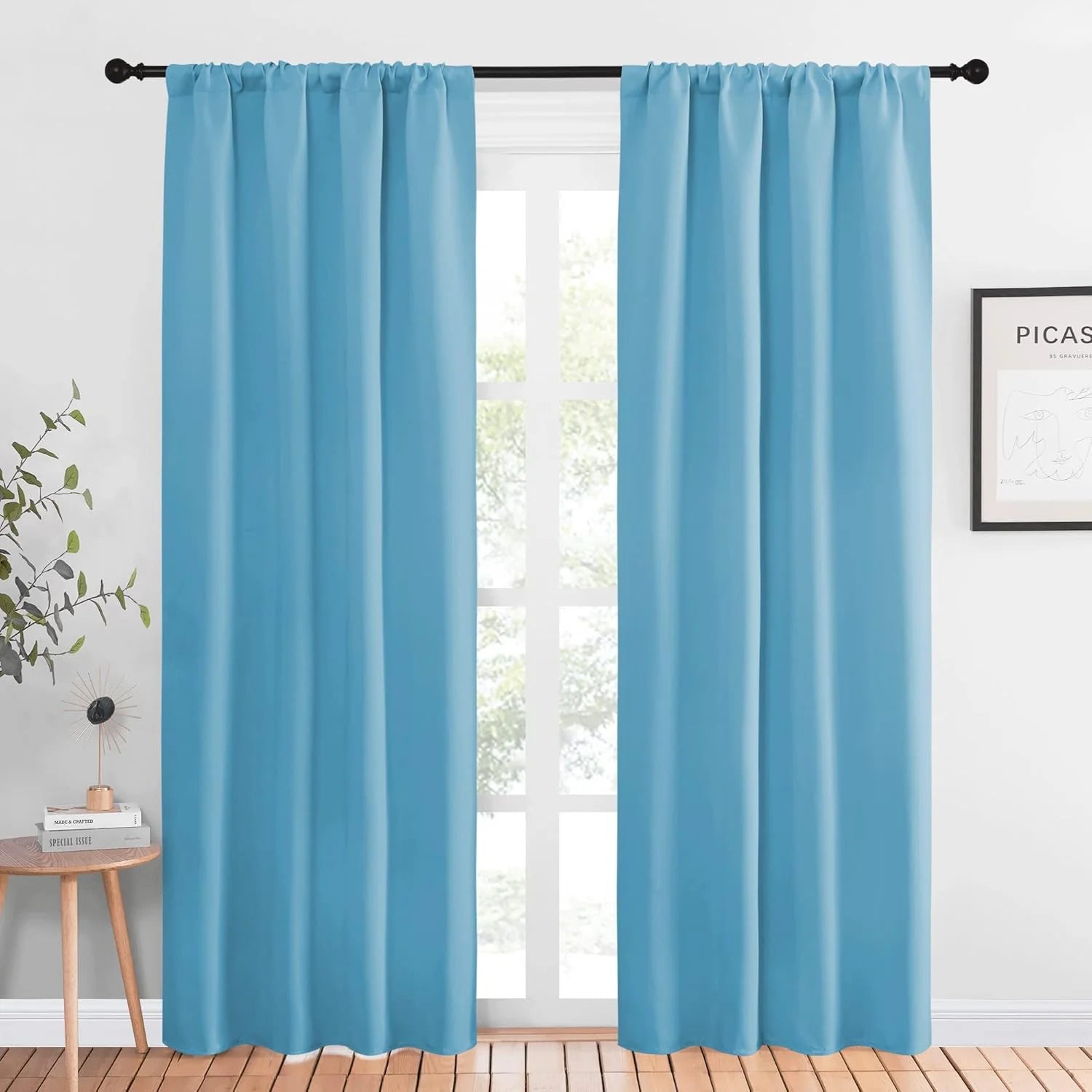 Sky blue solid rod pocket curtains hanging on a black curtain rod in a bright room