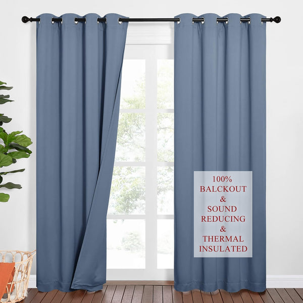 Slate blue grommet top blackout curtains hanging on a dark rod in front of a bright window.