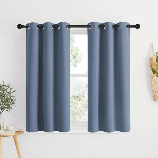 Two solid slate blue blackout tier curtains with silver grommets hanging on a black rod over a window.