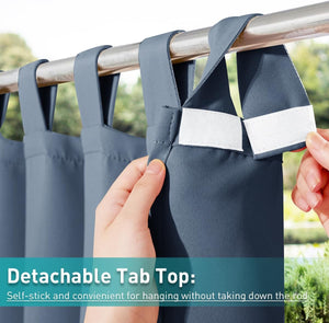 Close-up of slate blue detachable tab top curtains on a rod, with a hand opening the hook-and-loop fastener.