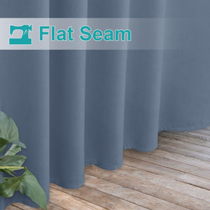 Close-up of slate blue curtains showcasing a neatly stitched flat seam hem, flowing to a light wooden floor.