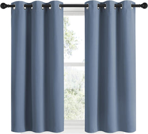 Pair of slate blue grommet top curtains hanging on a black rod over a window.