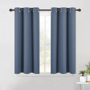 Pair of slate blue solid fabric grommet top curtains hanging on a bronze rod over a window.