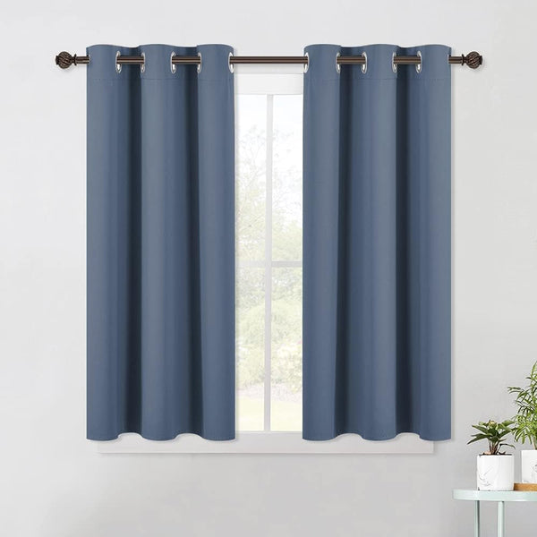 Pair of slate blue solid fabric grommet top curtains hanging on a bronze rod over a window.