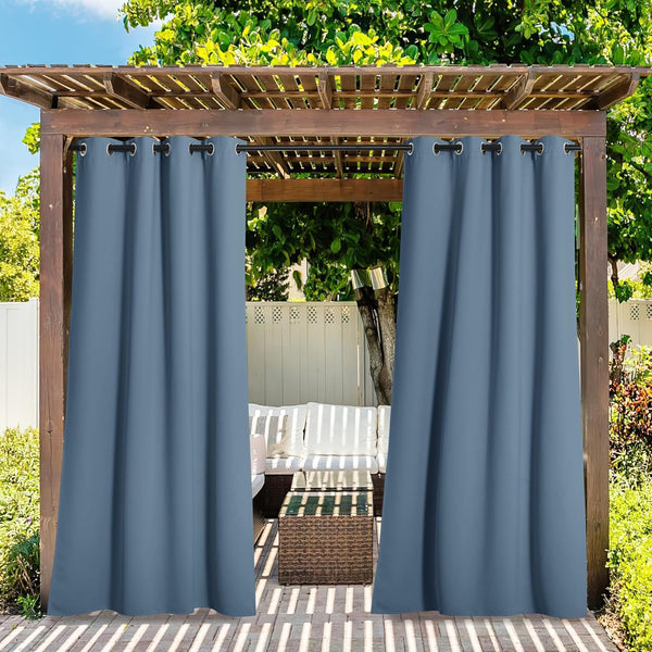 Two slate blue outdoor curtains with grommet tops hanging from a wooden pergola, revealing patio seating.